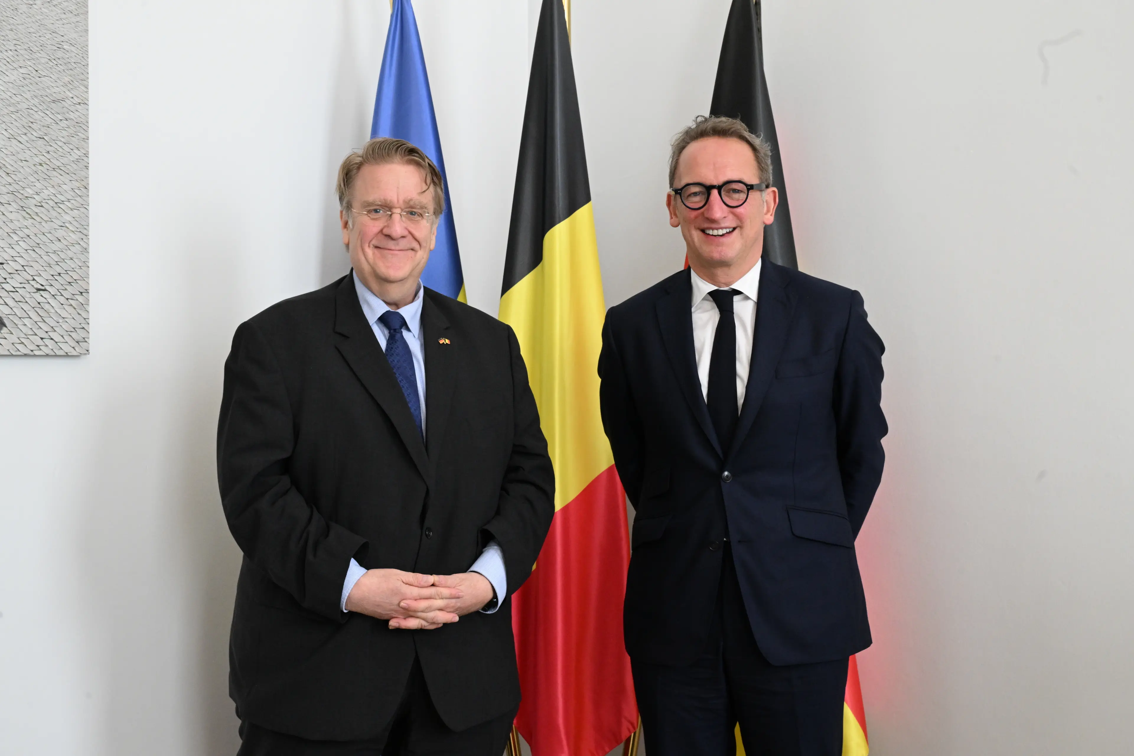Le Ministre-Président bruxellois et l’Ambassadeur d’Allemagne, posant debout devant les drapeaux bruxellois, belge et allemand