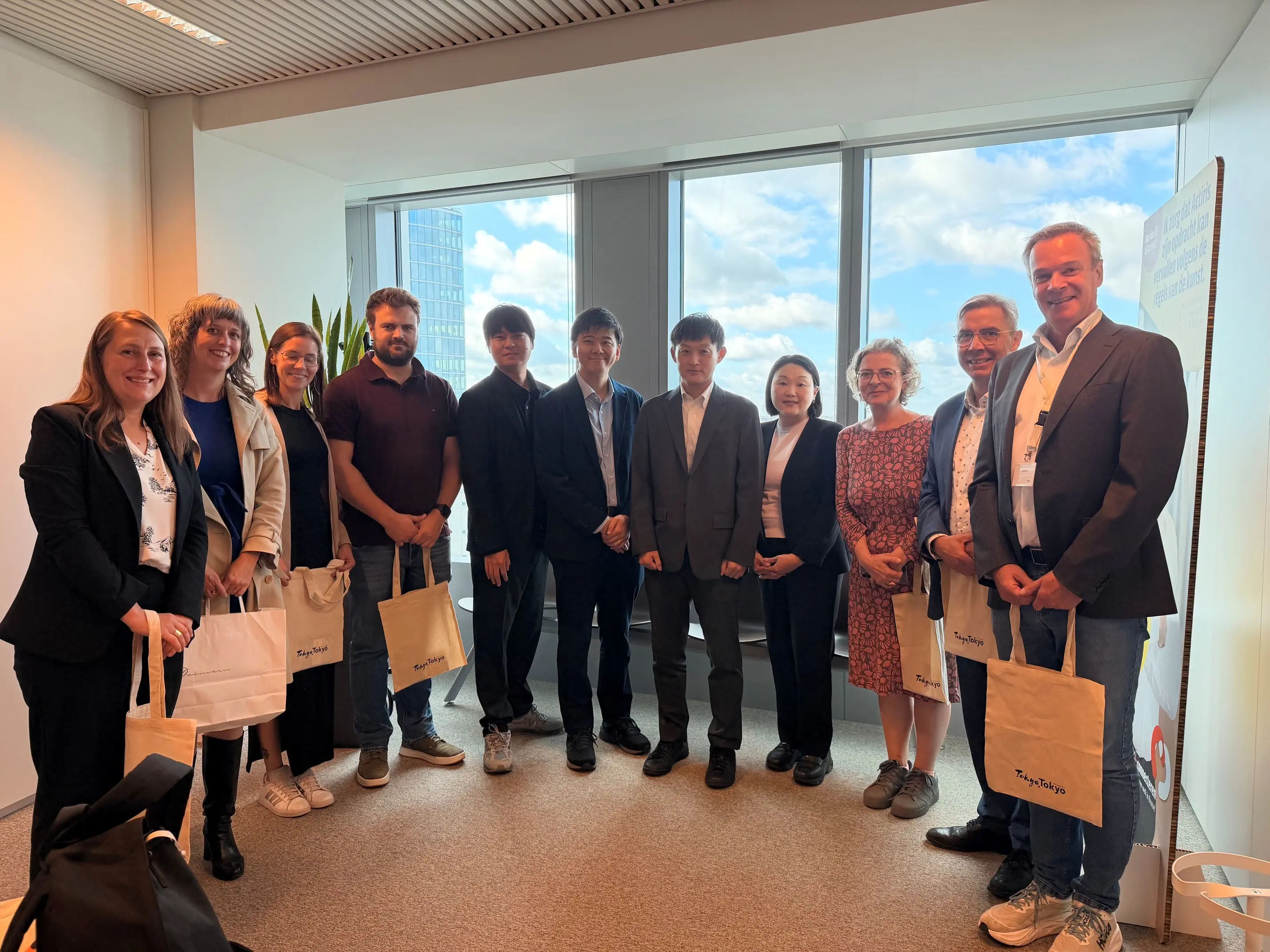 Tokyo and Brussels representatives standing for a group photo in a room