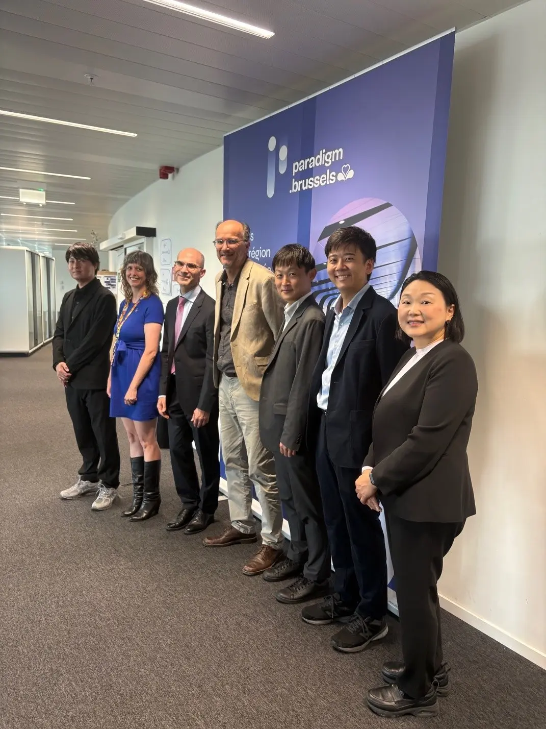Tokyo and Brussels representatives standing for a group photo in front of a Paradigm-branded panel